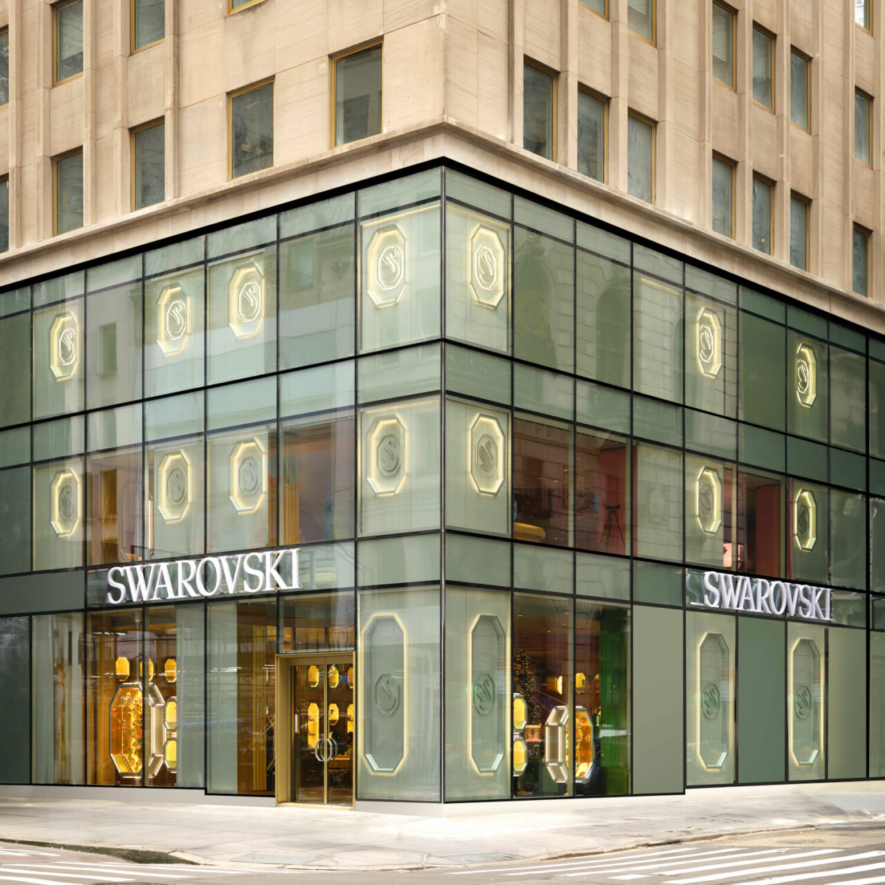 Street-level view of a multi-story Swarovski store on a corner, featuring architectural lighting that highlights the building’s façade and interior jewelry displays.